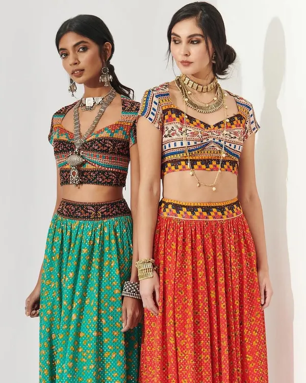 A vibrant shot of two models in colorful, mirror-work lehengas, perfect for a Navratri-themed sangeet or Mehendi. The makeup is fresh and glowing, with defined eyes that complement the bohemian-inspired styling.