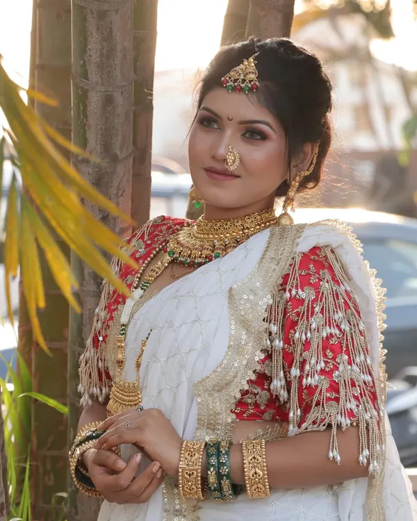 A stunning Maharashtrian bride in a white saree with a contrasting red blouse. The look is completed with a traditional nath and gold jewellery, creating a perfect blend of modern elegance and timeless tradition.