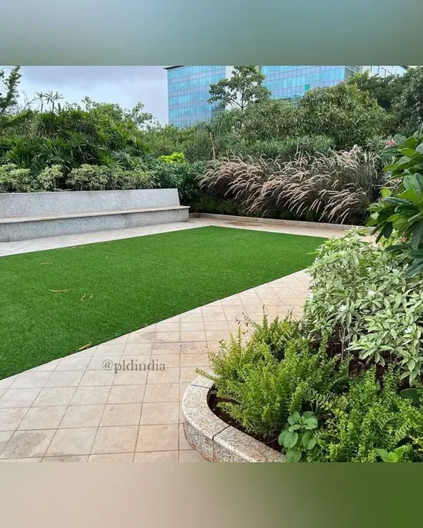 A view of the corporate amenity space, showing the balance between a pristine lawn and lush, mixed-foliage planters. The curved concrete planter with built-in bench seating provides a functional and aesthetic border for the green space.