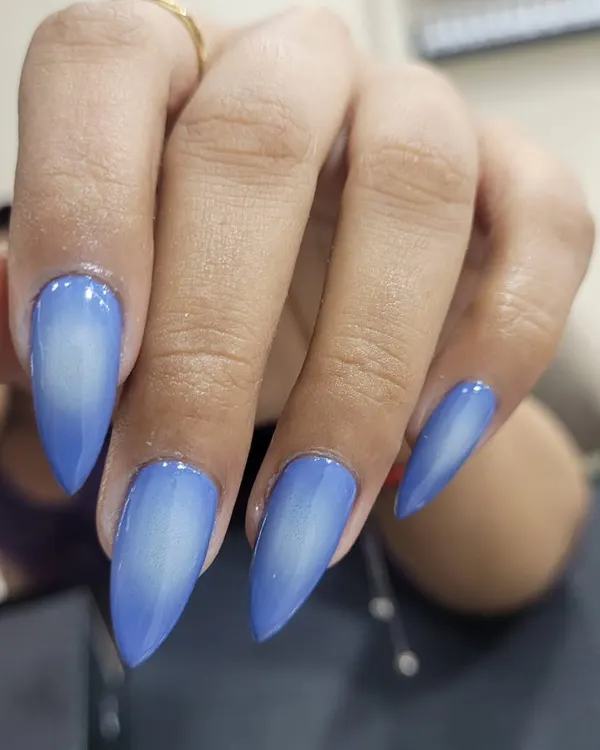 A striking airbrushed ombre effect on long stiletto nails. The vibrant blue fades into a soft white center, creating a bold and futuristic look.
