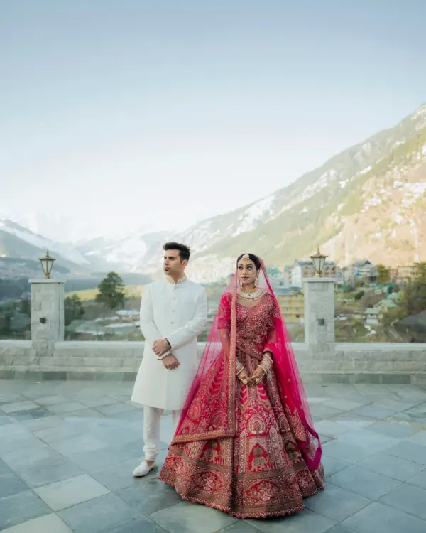 A portrait that speaks volumes. The couple stands against the breathtaking expanse of the Manali mountains, their regal wedding attire contrasting beautifully with the raw nature. This is the essence of a destination wedding.