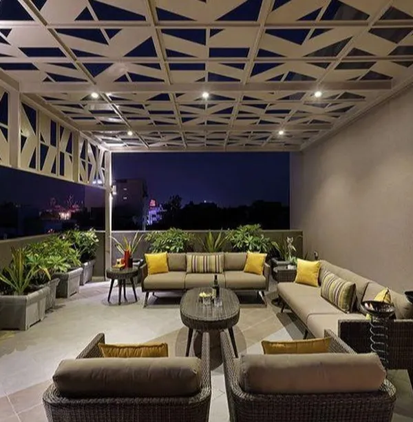 A modern terrace designed for evening entertainment. This space features a custom geometric-patterned pergola with integrated lighting, comfortable lounge seating, and large planters to create a sophisticated city-view retreat.
