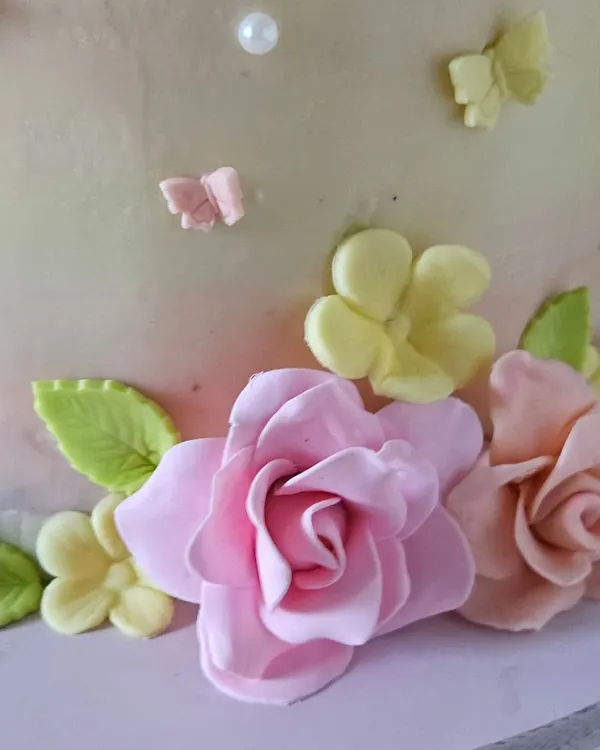 A close-up of the handcrafted sugar flowers from the enchanted garden cake. I shape and dust each petal by hand to create realistic and delicate blooms, like these pink roses and yellow blossoms.