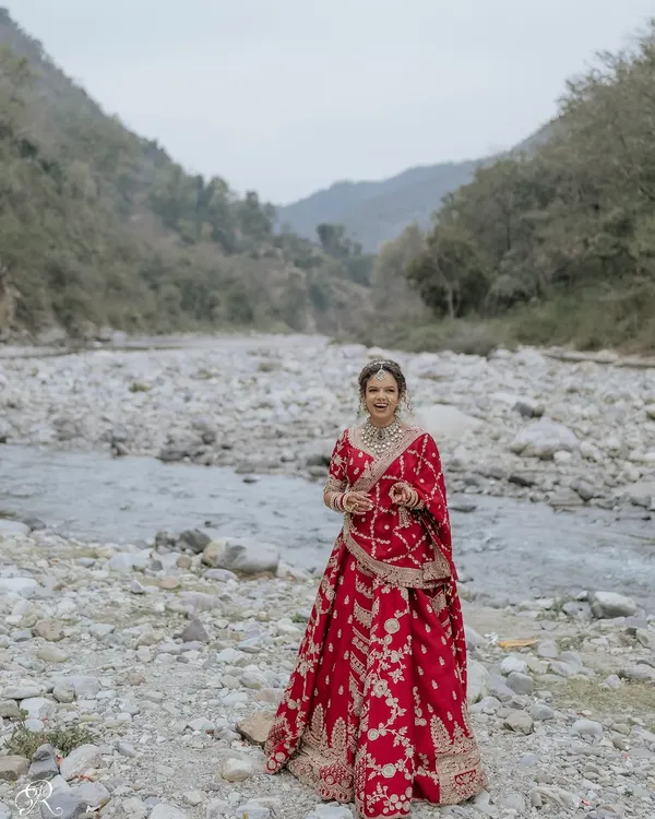 A stunning full-length portrait of the bride in her red lehenga, set against the majestic landscape of Rishikesh.