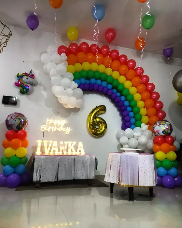 A bright and cheerful rainbow themed birthday party. This setup includes a large rainbow balloon arch, rainbow balloon pillars, a 'Happy Birthday' neon sign, and a unicorn foil balloon for extra magic.