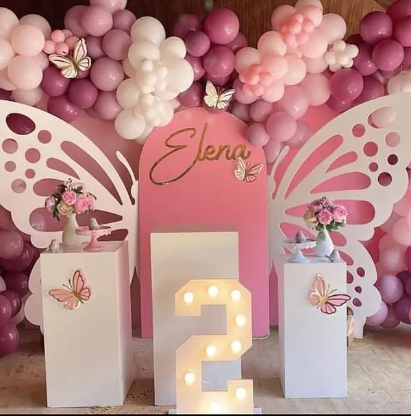 A stunning setup featuring large, white, laser-cut butterfly wings that create a perfect photo opportunity. The pink and lilac balloon arrangement and a light-up marquee number '2' make this an elegant and dreamy second birthday party.