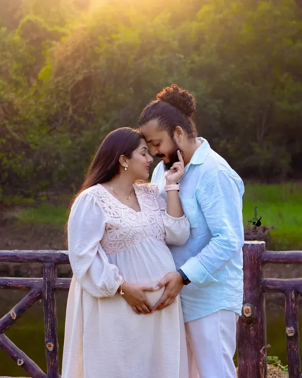 An intimate portrait of an expecting couple, framed by a rustic wooden fence and lush greenery. The warm sunset light adds a romantic glow, perfect for a natural light pregnancy photoshoot.