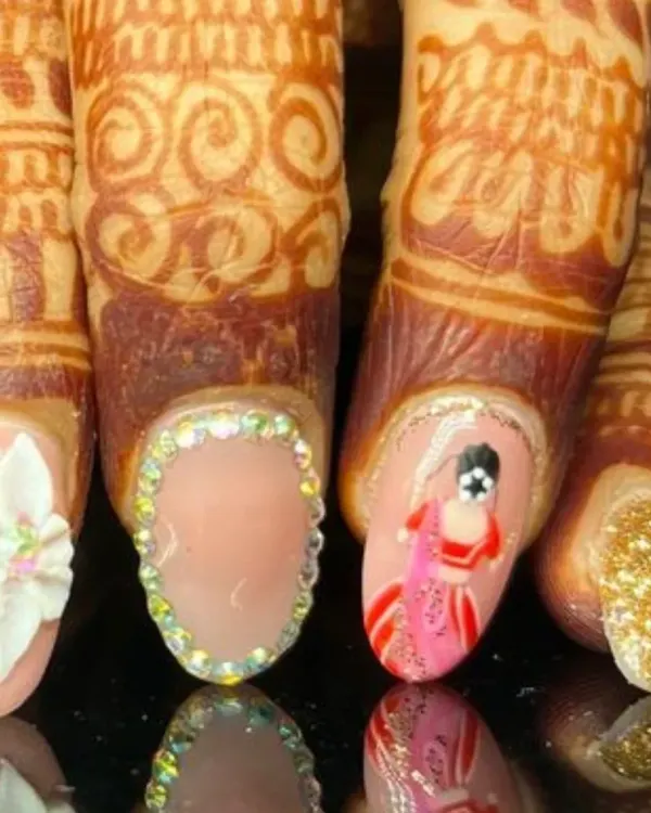 A close-up of the incredible detail on a bridal nail set, featuring a hand-painted bride, a 3D white flower, a full rhinestone border, and a gold glitter accent nail.