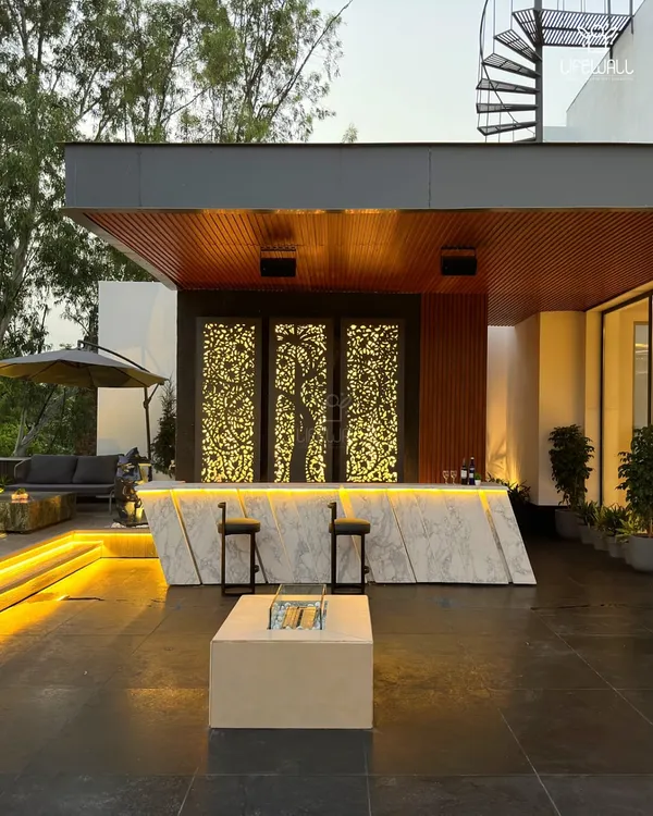This is a statement bar. It features a geometric marble front, a wooden backdrop with intricate, backlit laser-cut panels, and a fire pit table, creating an incredibly luxurious atmosphere.