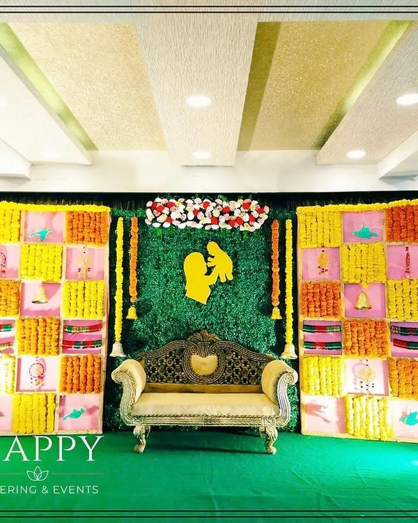 A traditional backdrop for a Seemantham or baby shower ceremony. The design features a colorful grid of fabric panels with marigolds and a central greenery wall.