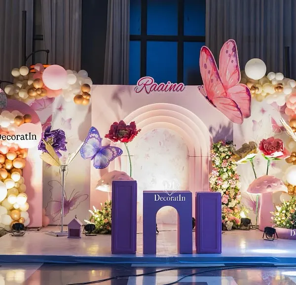 This enchanting stage setup for a butterfly-themed first birthday features a custom arched backdrop, larger-than-life 3D butterflies and flowers, and a beautiful balloon garland. It's the perfect spot for cake cutting and creating lasting memories.