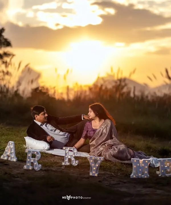 A perfect sunset proposal scene. I set up "Marry Me" light-up letters and a picnic blanket for this couple's special moment in a grassy field overlooking the mountains.