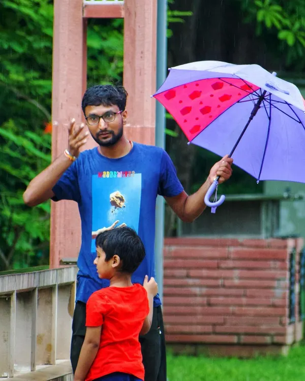 A candid moment between a father and son on a rainy day. The father gestures while holding an umbrella, showing a simple, everyday interaction that is full of narrative.
