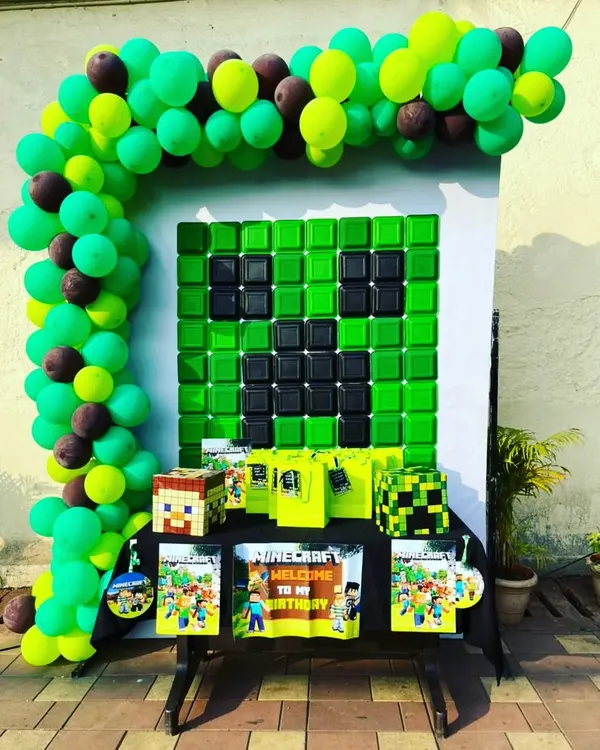 A creative Minecraft themed birthday party setup. The backdrop features a Creeper face made of balloons, with Minecraft-themed gift bags and props ready for the young gamers.