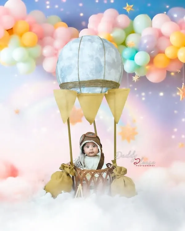 A whimsical hot air balloon setup for a sitter session, complete with a pilot cap, fluffy clouds, and a pastel balloon backdrop. This is one of my most requested creative milestone shoots.