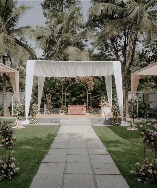 A wide view of an elegant daytime event we designed in a lush garden. The setup features a central stage with a minimalist gold arch, flanked by guest seating under pastel-draped canopies for a soft and romantic feel.