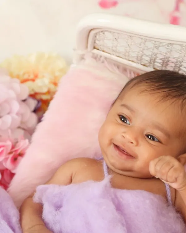 It's always a delight when a baby flashes a happy smile during the session. This candid moment captures a genuine expression of contentment amidst a bed of soft fabrics and flowers.