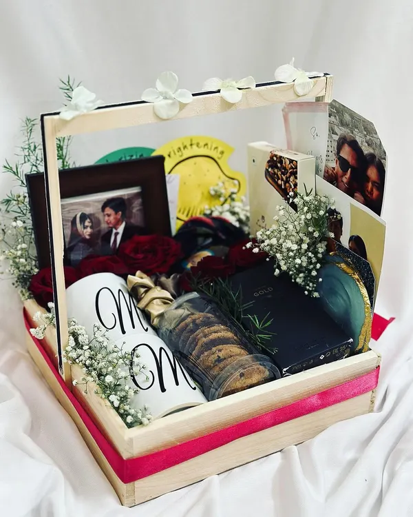 Celebrate their special day with a romantic anniversary hamper. This beautiful pinewood basket is filled with a personalized "Mr & Mrs" mug, a photo frame, fresh red roses, cookies, and other treats.
