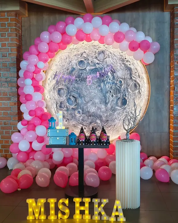 **Hero Item:** We believe in creating parties that are out of this world. This 'Love You to the Moon and Back' theme for a first birthday features a custom-made moon backdrop, a pink and white balloon arch, and marquee lights, turning a simple space into a celestial dreamscape.