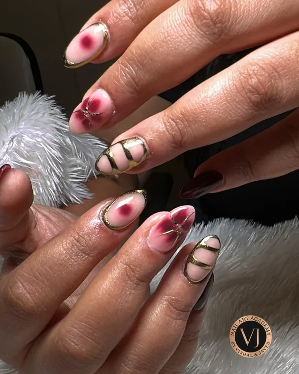 This design is a true work of art, combining multiple techniques. It features a blush pink base with hand-painted wine-red florals, alongside nails with bold, graphic gold chrome lines for a modern, edgy contrast.
