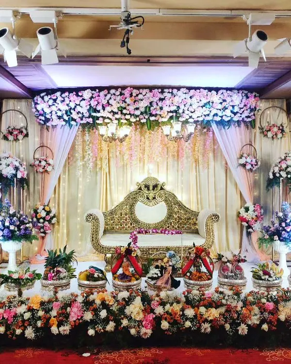 Here is a lavish wedding reception stage I designed. The setup features a beautiful floral canopy with hanging chandeliers over an ornate golden sofa, with a sea of my decorative trays and flower arrangements creating a truly grand display.