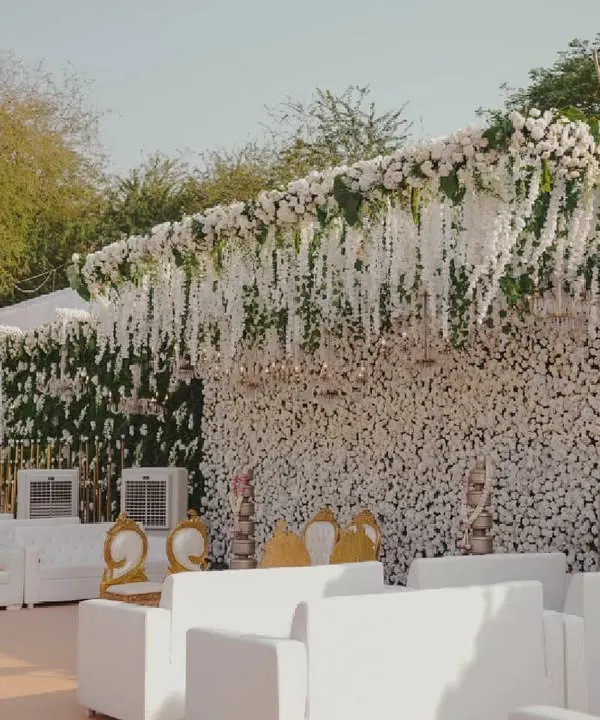A breathtaking wedding stage completely adorned with white carnations and hanging wisteria, creating a dreamy, cloud-like effect for an outdoor ceremony.