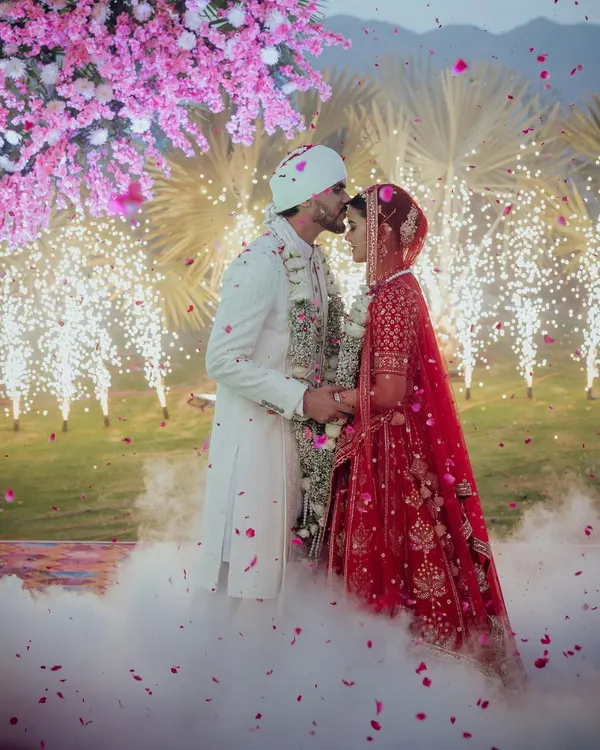 A fairytale moment as the groom kisses his bride's forehead, enveloped in a magical cloud and surrounded by the sparkle of fireworks and a shower of pink blossoms.