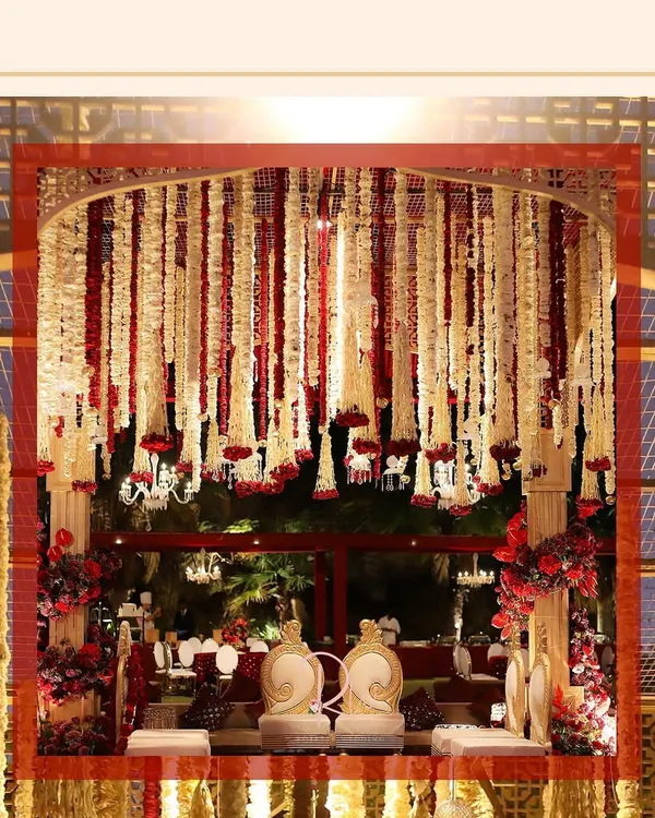 A view of the traditional red and white floral mandap from the side. The structure is covered in strings of tuberose and red carnations, creating a dense, fragrant canopy.