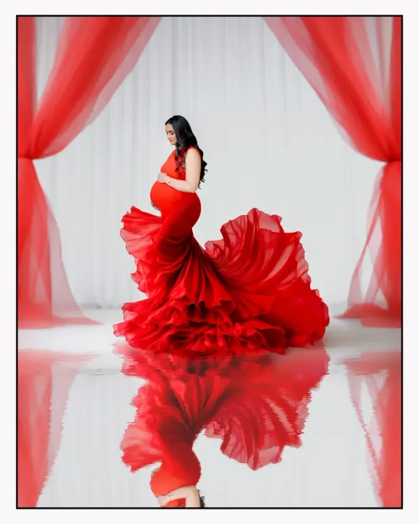 A dramatic solo portrait in our studio featuring a vibrant red maternity gown with a long, ruffled trail, creating a stunning reflection on the floor. This style is perfect for mothers-to-be who want a bold and glamorous photoshoot.