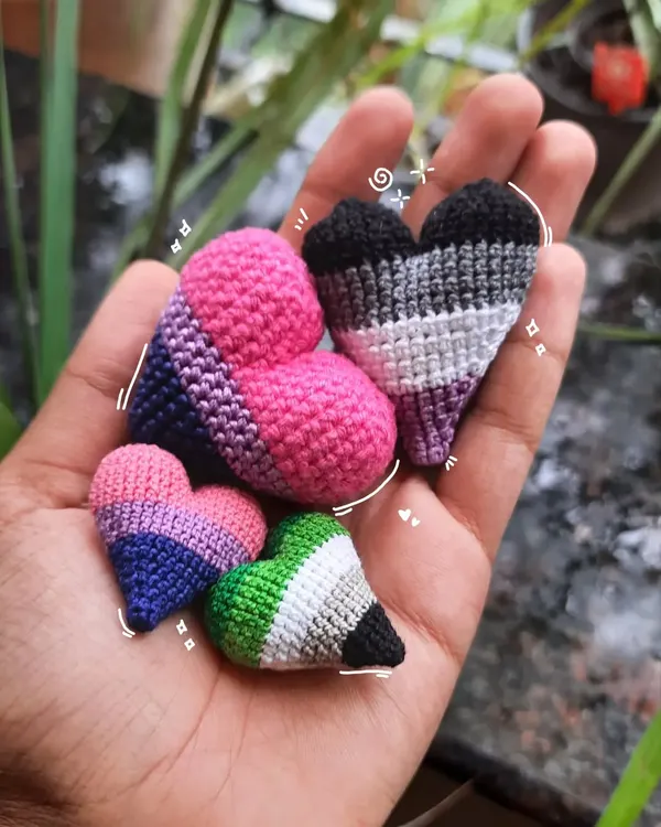 A handful of my crochet pride hearts, showing the bisexual, asexual, and aromantic flag colors. These can be made into pins, keychains, or earrings to wear your pride.