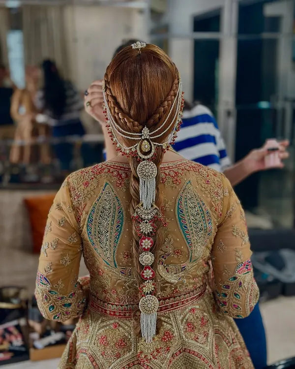 A stunningly detailed traditional braid for a wedding. This look features intricate side braids leading into the main plait, which is heavily adorned with pearl and kundan hair jewelry, including a passa.
