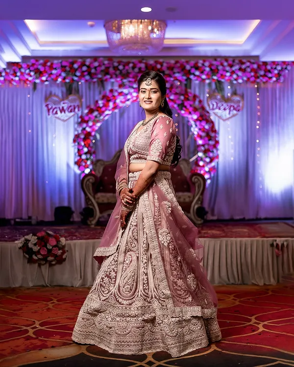 A full-length portrait of the bride, Deepa, showcasing her magnificent lehenga and the grand decor of the wedding venue.