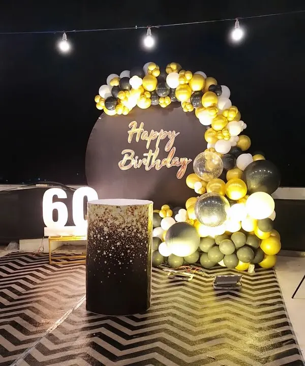 A sophisticated black, white, and gold theme for a 60th birthday. The setup includes a circular backdrop, marquee numbers, and a glittery plinth for the cake.