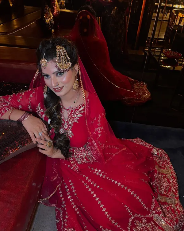 A full-length view of the traditional Pakistani bridal look. The magnificent red anarkali, paired with heavy gold jewelry and a long braid, creates an image of pure regality and grace.