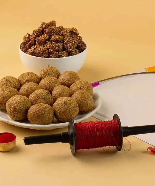 A classic, well-lit photograph capturing the essence of Makar Sankranti. The composition balances traditional sweets like ladoo with festive elements, shot against a warm, seamless beige background to make the colors pop.