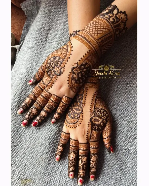 A fancy back-hand henna design featuring graceful peacock motifs. The use of negative space and detailed feather work makes the peacocks stand out beautifully.