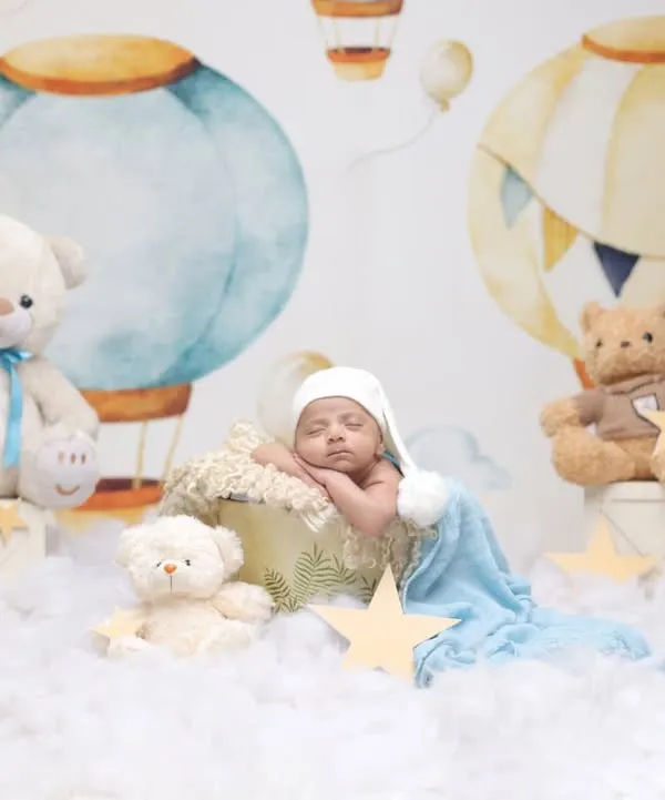 A dreamy hot air balloon adventure. This whimsical setup features a baby sleeping in a basket amongst the clouds, surrounded by teddy bears and stars.