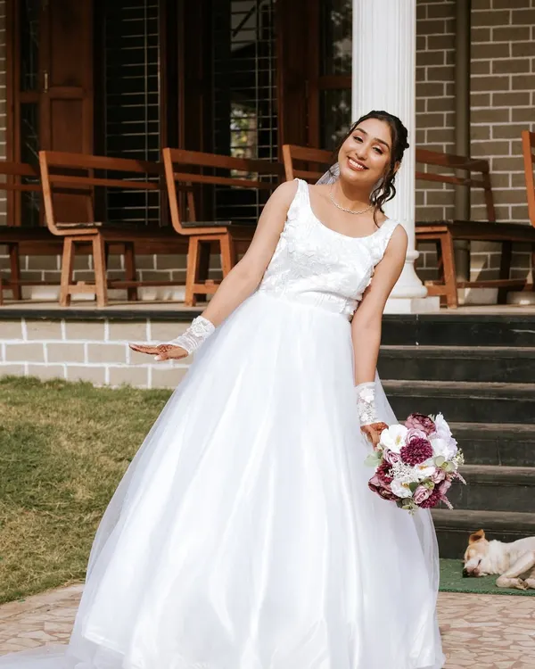 A joyful Catholic bride, Priyanka, in her beautiful white gown, holding a bouquet. Her makeup is fresh, radiant, and picture-perfect.