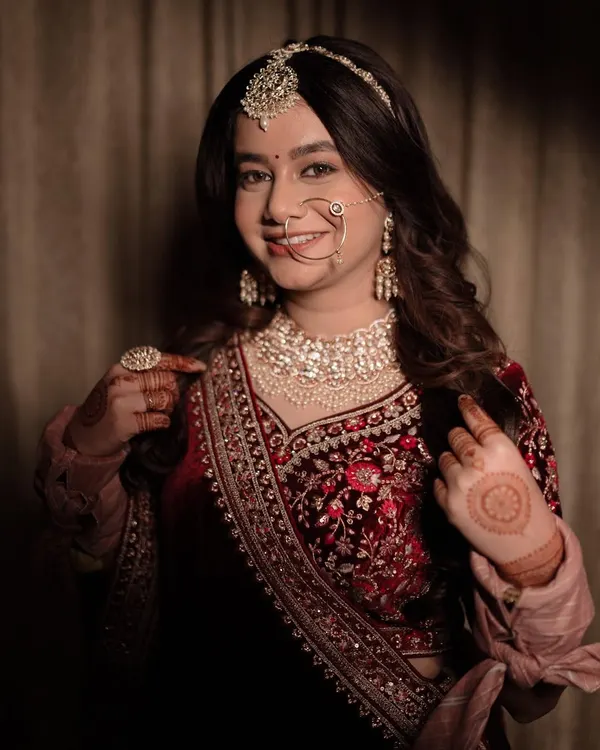 A happy bride showing off her intricate henna and stunning jewelry. This mid-shot captures her personality and the beautiful details of her velvet blouse and heavy embroidery, a perfect memory from her wedding day.