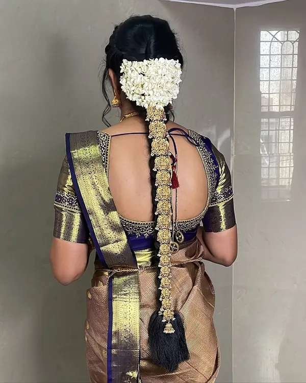 A classic South Indian bridal hairstyle. This long braid is adorned with traditional gold jada billai and fresh jasmine flowers, creating a truly regal look.