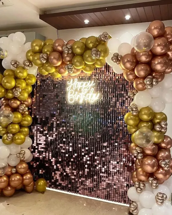 This is a full view of the rose gold sequin wall with a balloon garland. The combination of chrome gold, rose gold, and white balloons creates a rich, celebratory feel. The 'Happy Birthday' neon sign adds a warm, inviting light, perfect for evening parties.