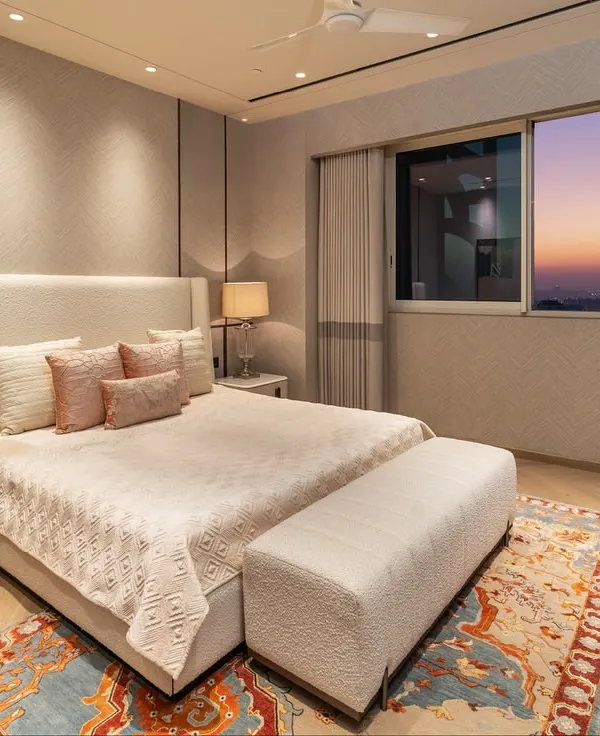 This guest bedroom in a Gurugram residence is designed for comfort and style. The soft pastel furnishings and artwork are complemented by a rich, dark veneer wall panel that adds contrast and depth, creating a warm and inviting atmosphere.