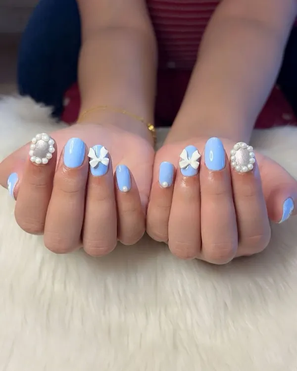A classic coquette nail set. This design features a soft baby blue polish with hand-sculpted 3D white bows and elegant pearl-framed accent nails for a touch of vintage charm.