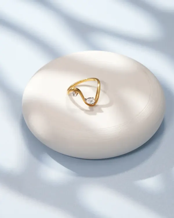A minimalist shot of a delicate gold ring on a white pedestal, with soft, leaf-like shadows. This elegant and serene composition is perfect for fine jewellery brands.