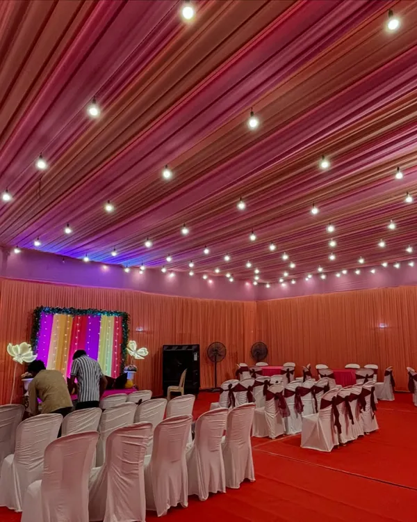 An indoor Mehendi setup with a colorful striped backdrop. We arranged seating for guests with simple white covers and maroon bows, keeping the focus on the vibrant stage.