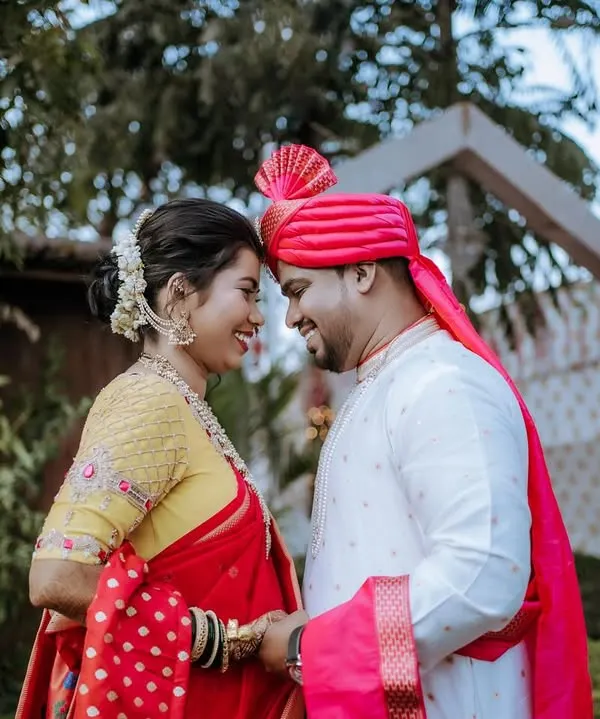 A sweet and romantic moment between a newly married couple. The groom wears a vibrant pink pheta, and their gentle forehead touch captures the love and happiness of the day.