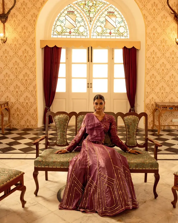 A wide shot from a brand campaign, establishing the regal atmosphere. The model is centered to command attention, showcasing the full silhouette of the purple gown against the palace's classic interior design.