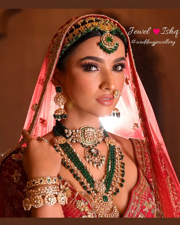 A close-up of a classic bridal look. The layered emerald bead necklaces, Kundan choker, and matching mathapatti create a majestic frame for the bride's face, perfect for a traditional wedding ceremony.
