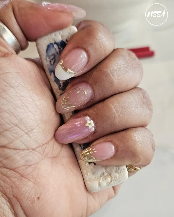A beautiful example of a modern, elegant manicure. This set features a mix of French tips with a gold chrome line, a sheer pink with a single floral gem, and a subtle gold flake accent.