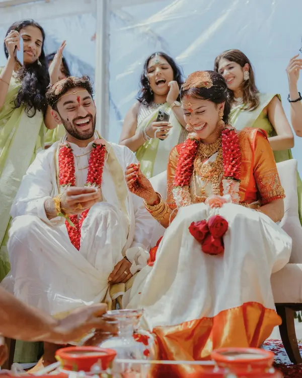 A candid and joyful moment from a South Indian wedding, where the couple and their friends are laughing during a ceremony.